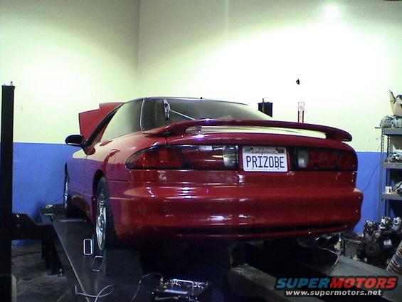 Red coupe on a lift, rear view. California license plate reads PRIZOBE