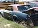 1968 Ford Coupe - A weathered Ford Mustang coupe sits in a junkyard, showing signs of significant disrepair and missing components.