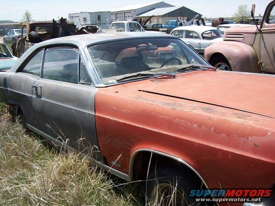 Side view of a two-tone coupe, front half is orange, rear half is gray. It's in a junkyard with other cars