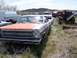 1968 Ford Coupe - A weathered 1966 Ford sits in a junkyard with other vehicles visible in the background under a cloudy sky.