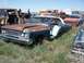 1968 Ford Coupe - A rusty teal and white coupe sits in a junkyard, its front end visible with a prominent grille and dual headlights.