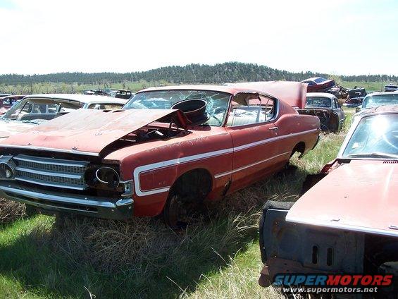 Red coupe with white stripe, hood up, broken windshield, in a junkyard with other cars