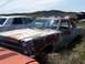 1968 Ford Coupe - A heavily rusted 1966 Ford Fairlane coupe sits in a junkyard, surrounded by overgrown grass and other vehicles.
