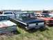1968 Ford Coupe - A black sedan sits in a junkyard, surrounded by other vehicles under a clear sky.