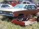 1968 Ford Coupe - This rusty sedan sits in a junkyard, surrounded by other vehicles and overgrown weeds.