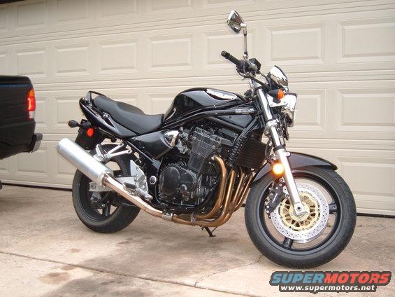 Black Suzuki Bandit motorcycle parked in front of a garage door. A black truck is partially visible on the left