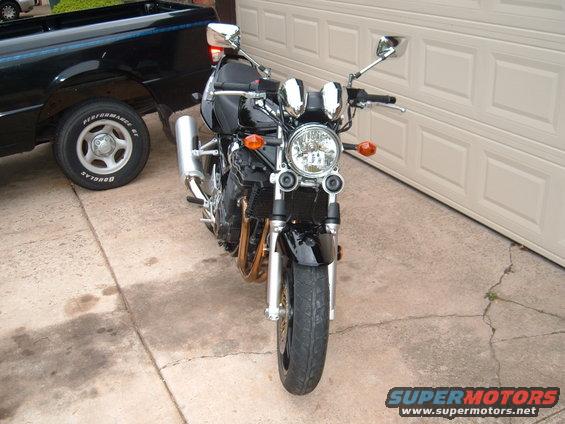 Front view of a black motorcycle parked on concrete next to a black pickup truck. Garage door in background