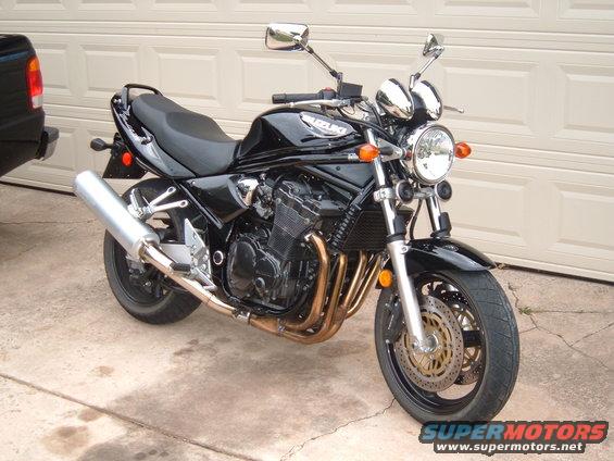 Black Suzuki Bandit motorcycle parked in front of a garage door. A black pickup truck is partially visible on the left