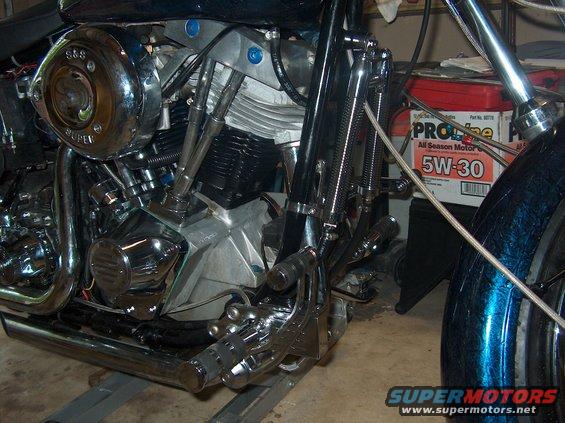 Motorcycle engine with S&S Super air cleaner, chrome exhaust pipes, and foot controls. Oil container visible in background