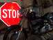 1976 Harley-Davidson Super Glide - A black motorcycle is parked in front of a red stop sign, with various signs and equipment visible in the background.
