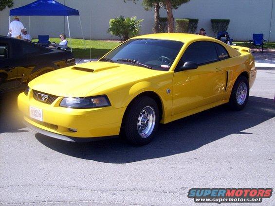 Yellow 2002 Ford Mustang parked next to a black car under a blue tent