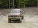 1979 Ford Bronco - This red pickup truck navigates a challenging muddy course, its tires deep in the mire.