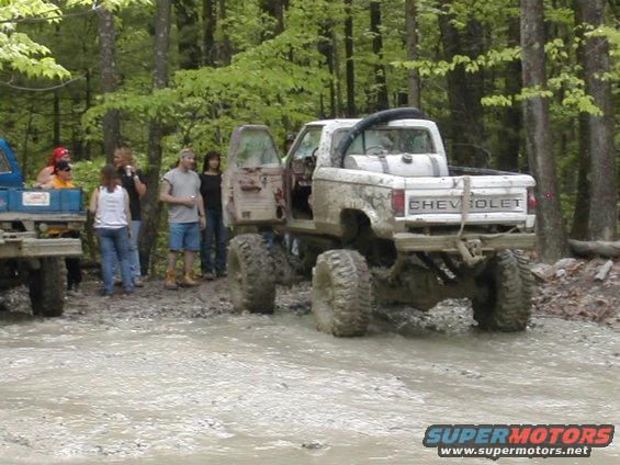 Muddy lifted pickup truck with 'CHEVROLET' on tailgate, rear view