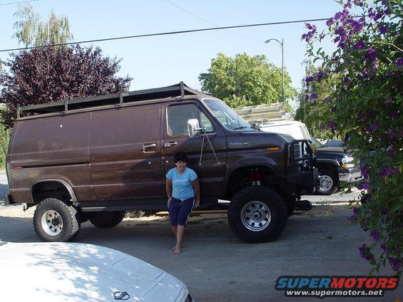 Brown van with roof rack and large off-road tires, parked outdoors