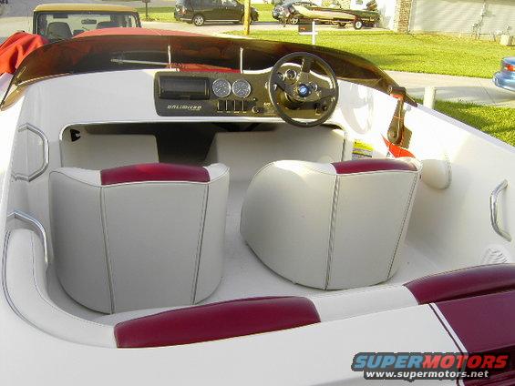 Boat interior with white seats and maroon accents. Steering wheel and dashboard visible