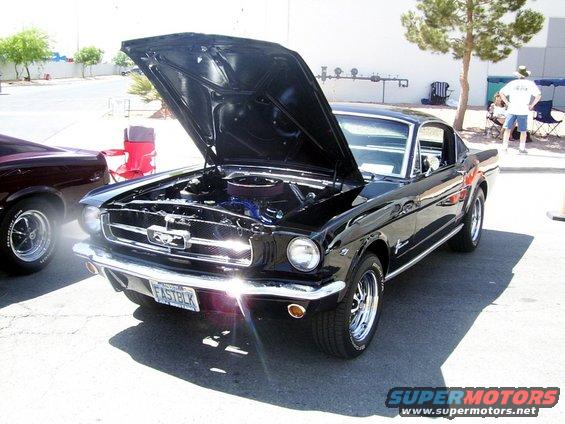 Black 1965 Ford Mustang coupe, hood open, chrome wheels, license plate reads FASTBLK