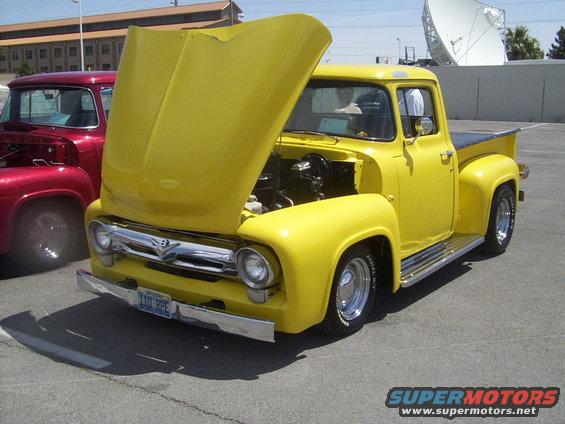 Yellow 1956 Ford F-100 pickup with hood open, parked next to a red truck