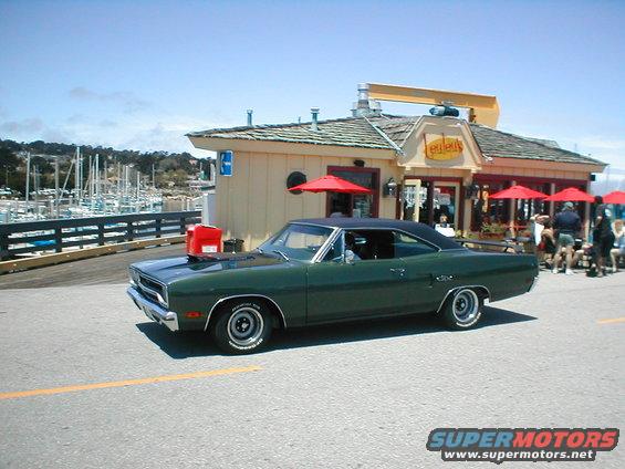 Green 1970 coupe with black vinyl roof parked by a seaside restaurant