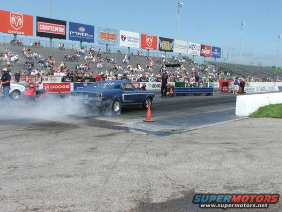 Blue 1969 Mustang doing a burnout on a drag strip with spectators in the stands
