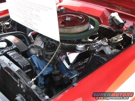 Red 1966 Ford Mustang engine bay with chrome details and a white information card