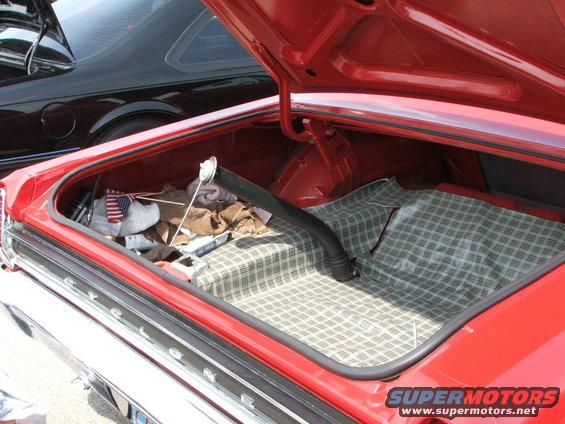 Red car trunk with plaid liner, American flag, and debris. A black car is visible behind it