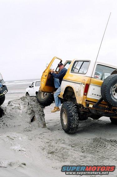 Guy climbing into yellow Ford Bronco on beach, another white Bronco behind it