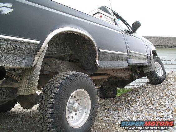 Side view of black pickup truck with large off-road tires climbing a gravel incline