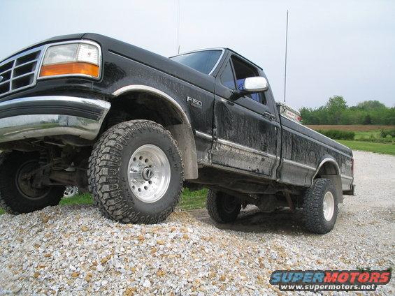 Black Ford F-150 pickup truck with off-road tires parked on a gravel pile