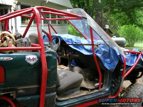 Green off-road vehicle with red roll cage, blue tarp covering dashboard, and exposed interior. "FAST" sticker visible on door