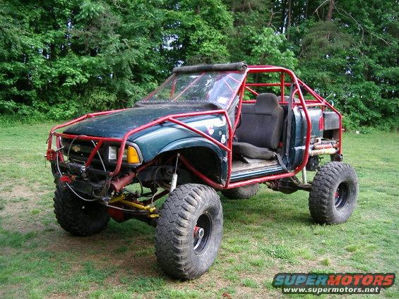 Green off-road vehicle with red roll cage, large tires, and open doors, parked on grass