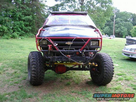 Off-road vehicle with large tires and red roll cage, front view