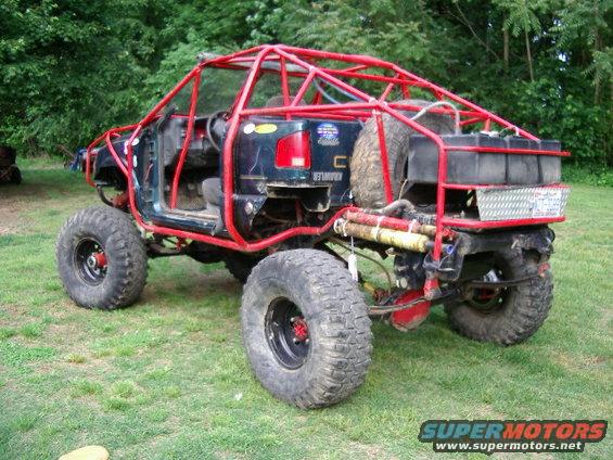 Modified off-road vehicle with red roll cage, large tires, and external fuel tanks