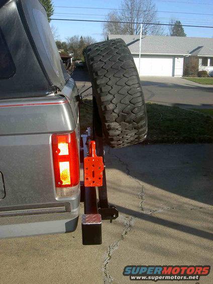 Rear view of a gray Ford Bronco with a spare tire mounted on a custom carrier. Shows the taillight and part of the soft top