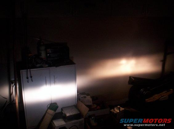 Headlights shine on a wall in a dimly lit garage, illuminating a cabinet and some boxes