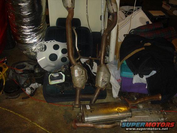 Car exhaust pipes and catalytic converters piled on the floor with a car seat and other parts
