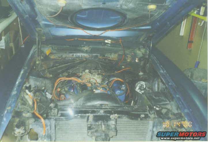 Blue car's engine bay with hood open, showing engine, wiring, and radiator