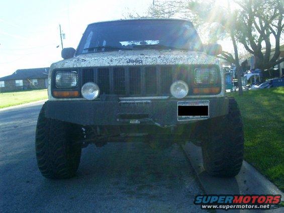 White Jeep Cherokee with aftermarket bumper and large tires, front view