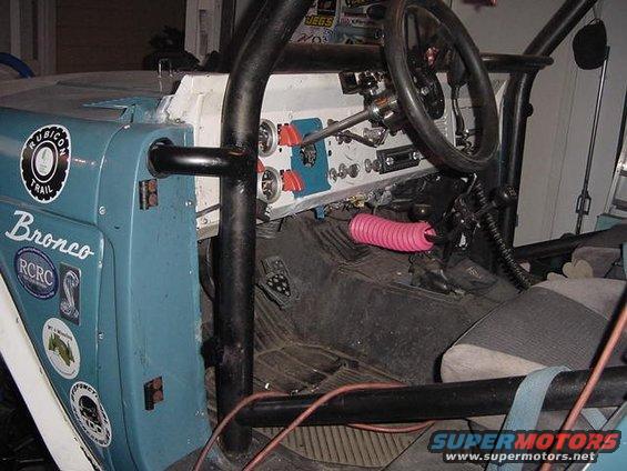 Interior of a blue off-road vehicle with a roll cage, custom dashboard, and various stickers on the door