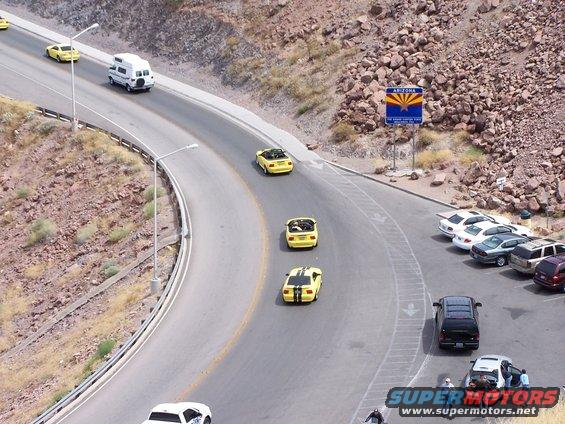 Yellow convertible sports cars driving on a scenic road near an Arizona sign