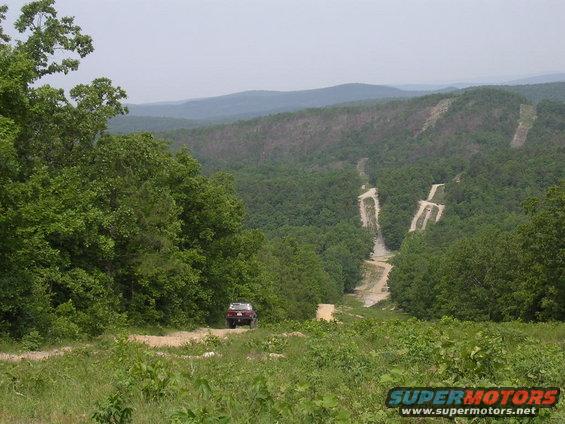 Red 1995 Jeep Cherokee from rear on dirt road with wooded hills