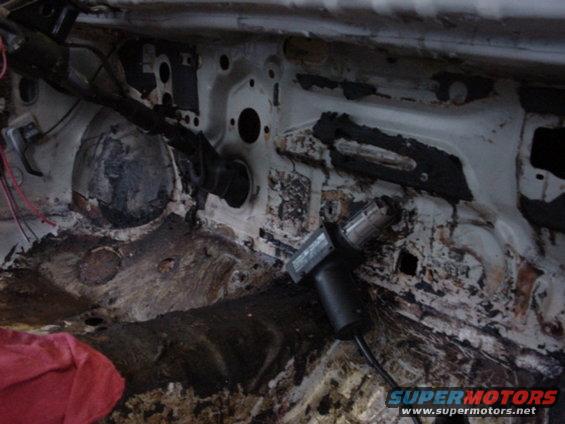 Car interior firewall area with exposed metal, wiring, and a heat gun. A red cloth is visible on the left