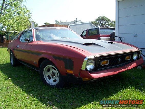 Red 1971 Ford Mustang coupe with black hood scoop and racing stripes parked on grass
