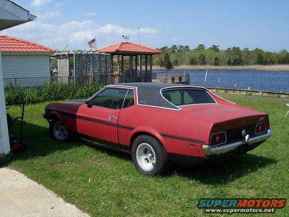Red coupe with black vinyl top parked on grass near water. Has a black stripe along the side