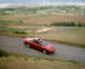 1996 Ford Probe - A red 1996 Ford Probe is captured from a high angle on a winding road with a scenic landscape in the background.