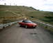 1996 Ford Probe - A red 1996 Ford Probe is captured in a three-quarter front view on a paved road, with a hilly landscape behind it.