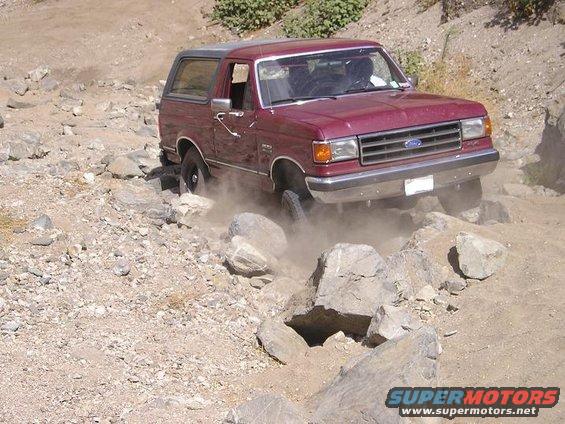 Maroon 1989 Ford Bronco navigating a rocky trail, kicking up dust