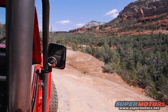 View from inside a red off-road vehicle looking out at a desert landscape with red rocks and pine trees