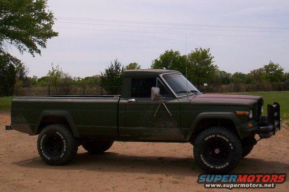 Green Jeep pickup truck with off-road tires parked on a dirt road