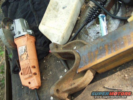 Orange angle grinder next to rusty metal brackets and a white plastic container on a wooden surface