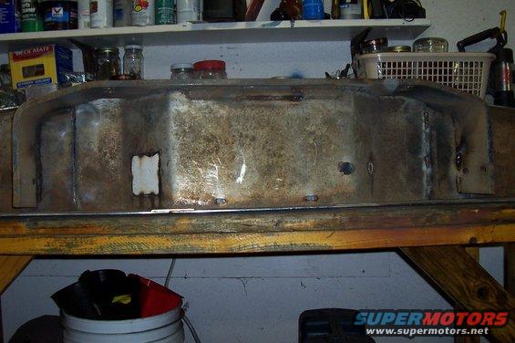 Welded metal fuel tank with some rust and patches, resting on a wooden workbench